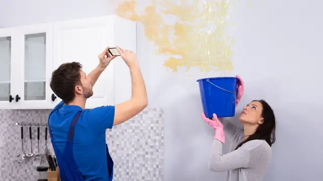 Renter photographing a water-stained wall while a partner holds a bucket