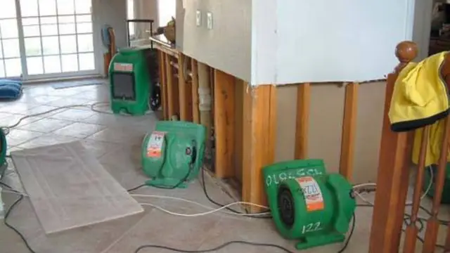 Green air movers drying a room where a wall has been opened for repair